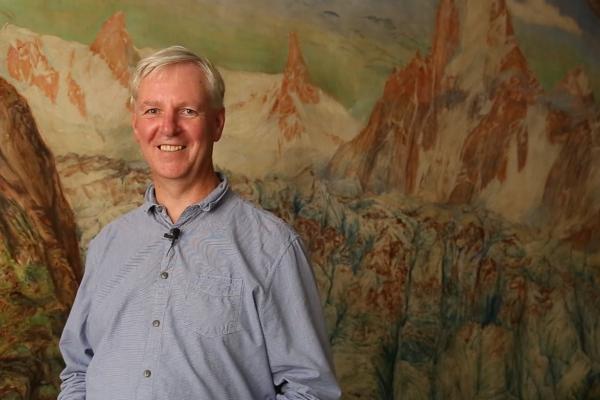 Steven Matthews in front of a painted mural of a mountain glacier