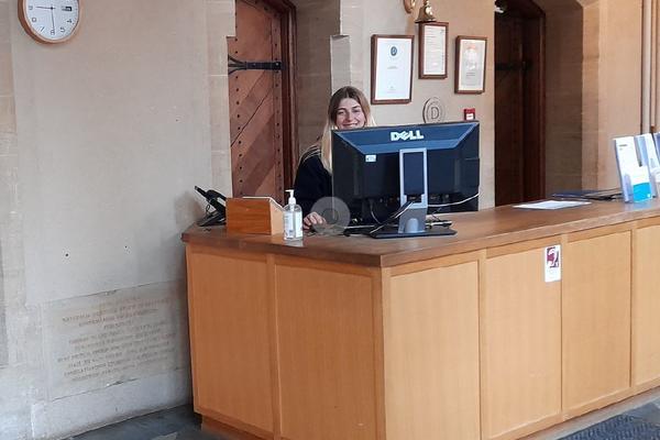 A wooden desk with a computer and a member of staff sitting behind it.