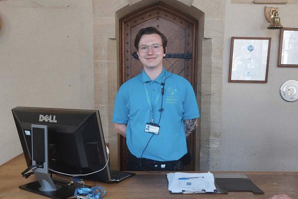 A Visitor Services Assistant wearing a light blue polo shirt with an embroidered logo