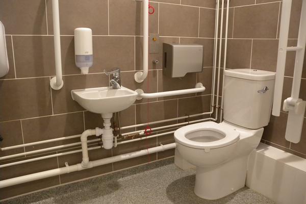 The North accessible toilet. The toilet is right hand transfer with toilet paper on the right, and a sink on the right wall just in front of the toilet